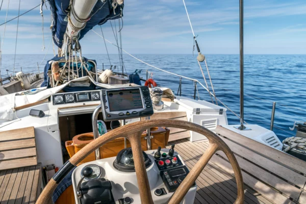 Blick über das Steuerrad einer Segelyacht auf offene See, Cockpit mit Navigationsdisplay und Kompass