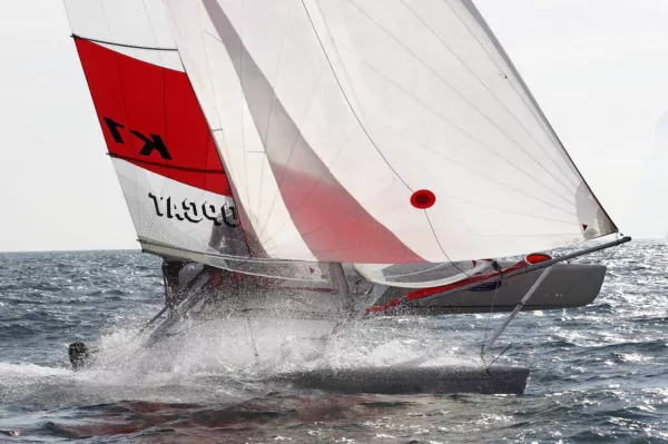 Schnell segelnder Katamaran mit rot-weißen Segeln bei hoher Geschwindigkeit auf dem Meer, Gischt spritzt