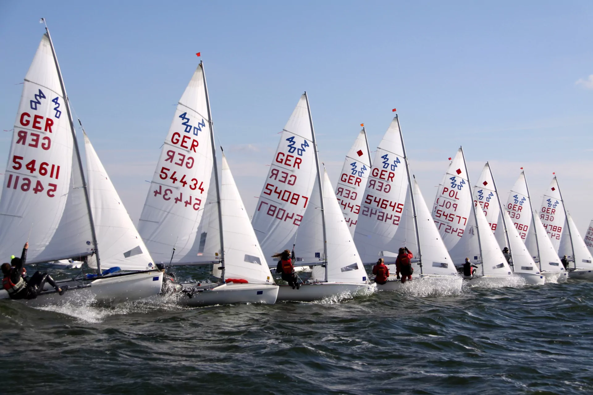 Segelregatta mit mehreren Jollen (GER) auf offenem Meer, weiße Segel, aktive Crews und leichte Wellen bei klarem Himmel