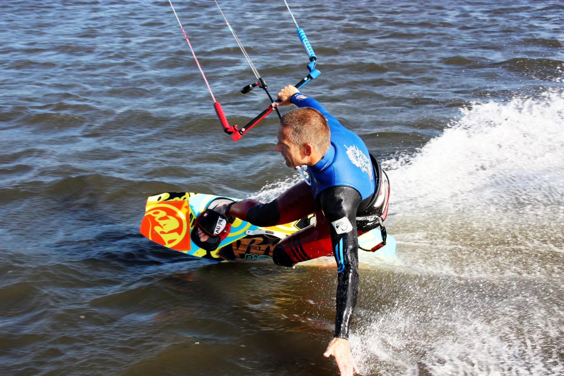 Kitesurfer auf buntem Kiteboard in Neoprenanzug fährt dicht über dem Wasser, spritzende Gischt, actionreicher Wassersport