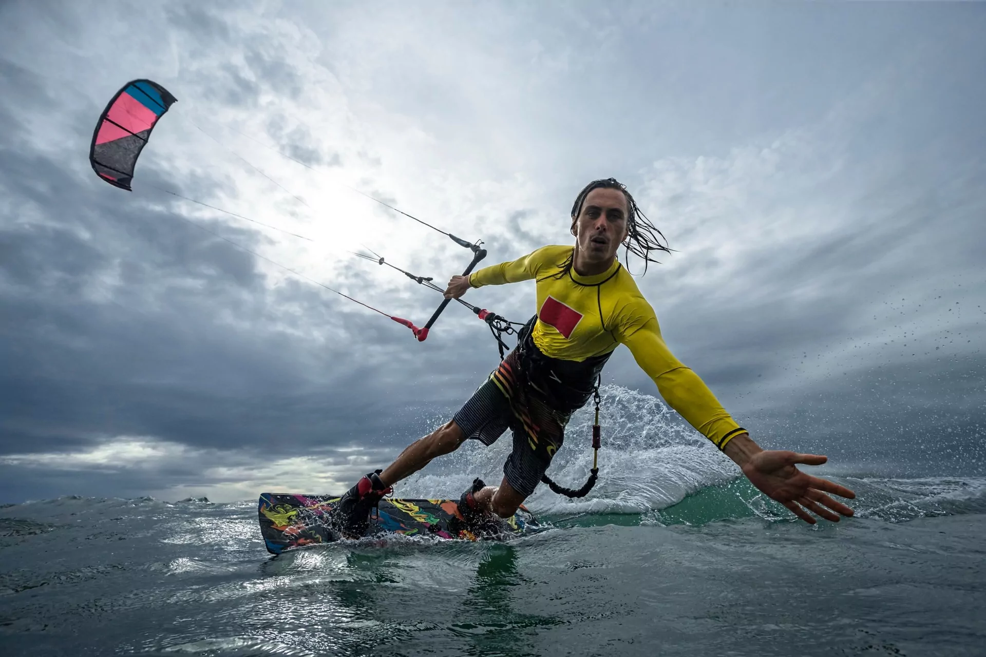 Action-Kitesurfer in gelbem Neopren steuert bunten Kite über raues Meer mit hohen Wellen