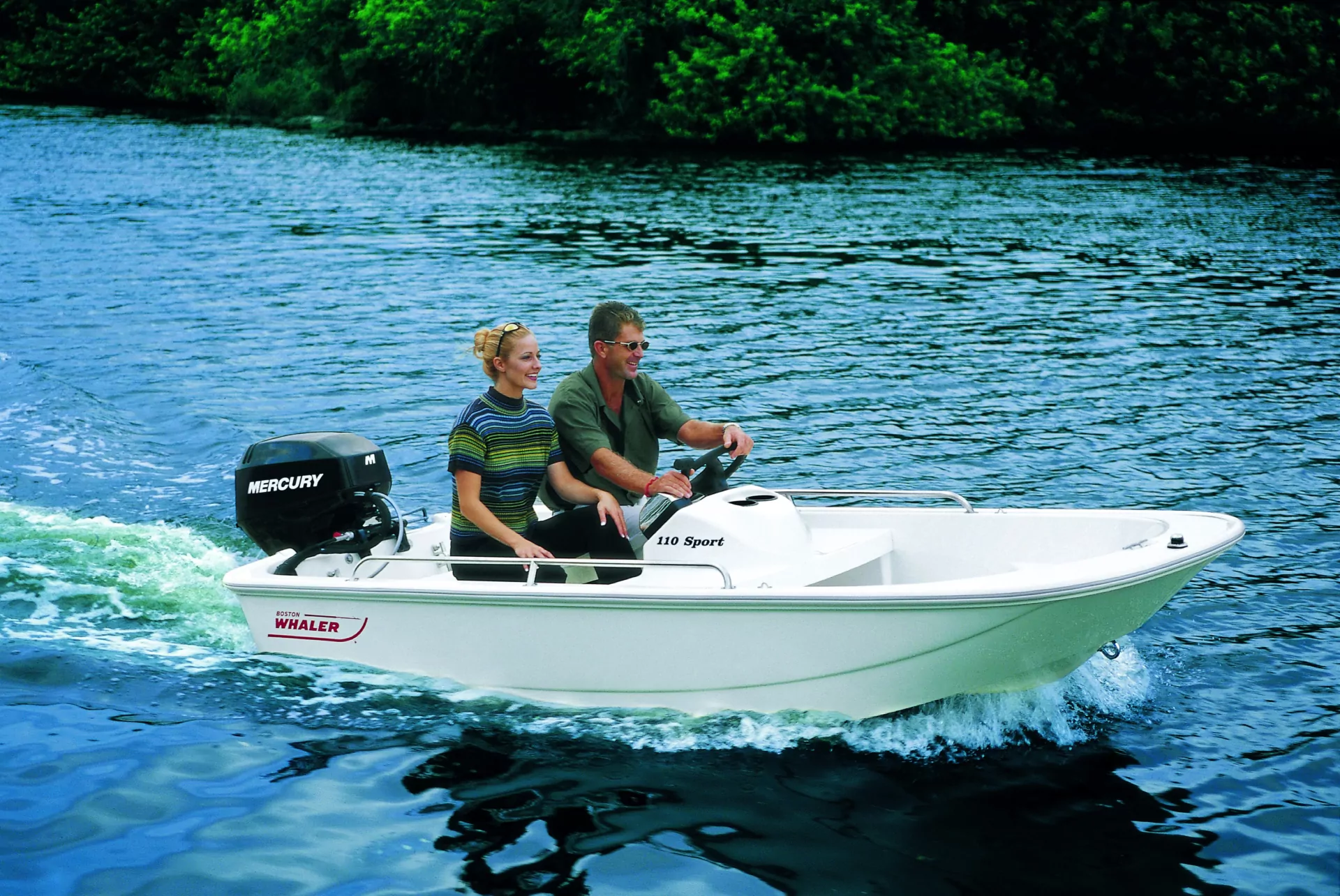 Paar in weißem Boston Whaler Motorboot fährt auf ruhigem blauem Wasser; Mann steuert, Frau lächelt