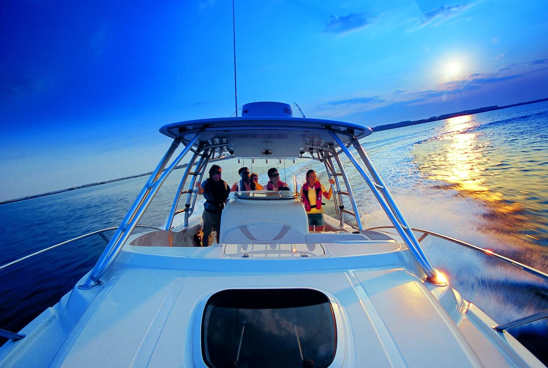 Motorboot bei Sonnenuntergang, Blick vom Bug auf offenes Meer mit Menschen in Rettungswesten