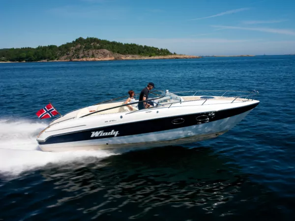 Schnellboot mit norwegischer Flagge fährt vor felsiger Küste, Paar an Bord, blaues Sommermeer