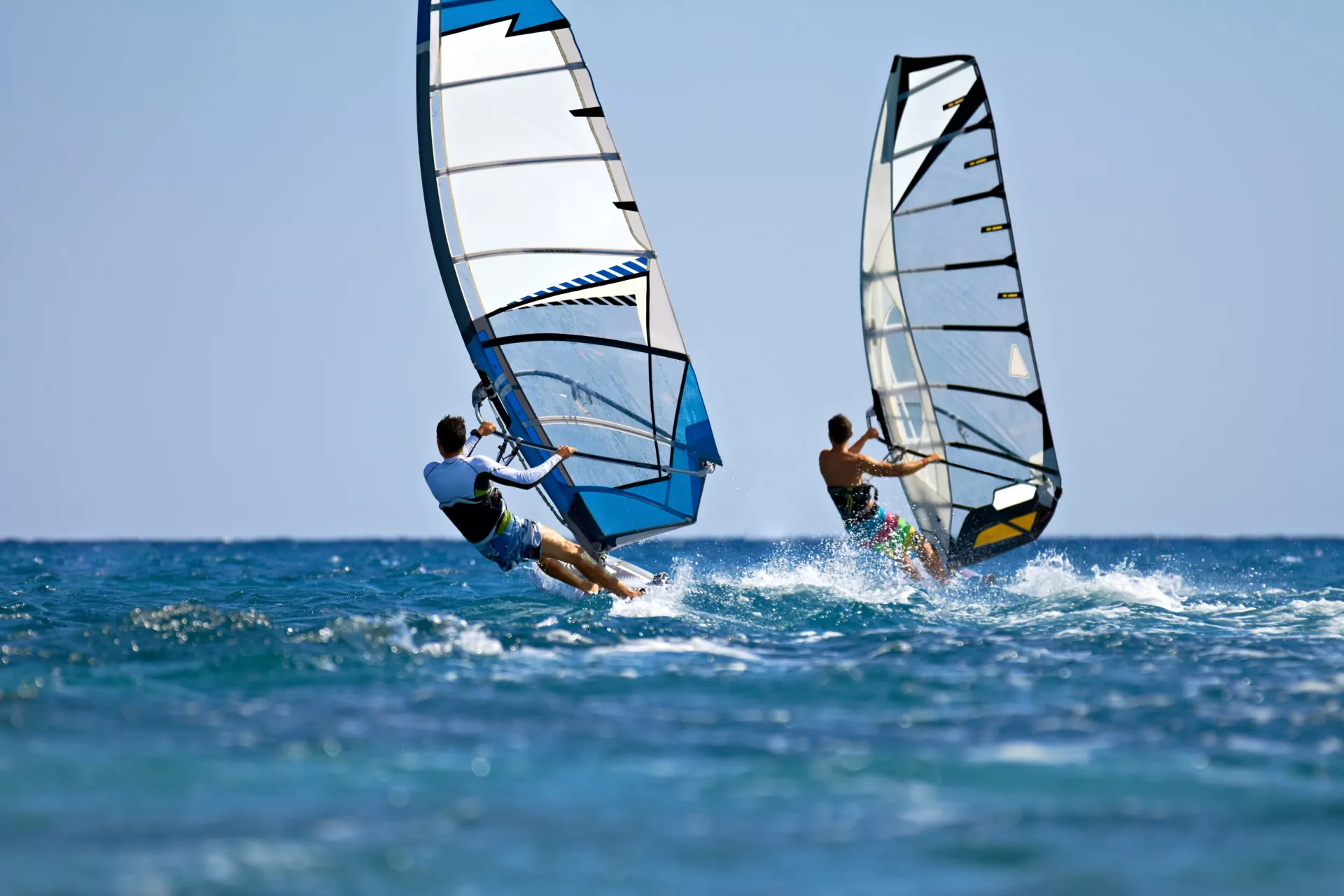 Zwei Windsurfer auf blauem Meer bei klarem Himmel, schnelle Segel und Spritzwasser – Windsurfen, Wassersport, Sommer