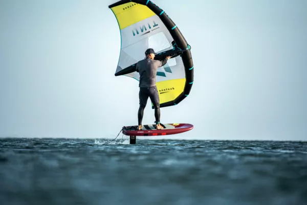 Wingfoil: Mann auf Foilboard mit gelb-schwarzem Wing über dem Meer beim Wassersport